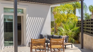 A covered patio with two wicker chairs and a small table, a grey sofa, and a glass door leading to an interior space.