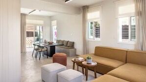 A modern living room with a sofa, ottomans, a dining table, and a kitchen area.