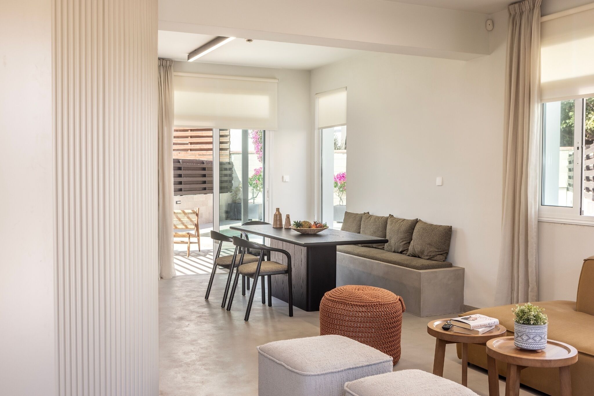 A modern living room with a dining area, a sofa, ottomans, and a small table with a plant.