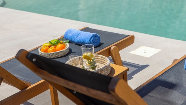 A poolside chair with a towel, a basket of oranges, and a glass of water.