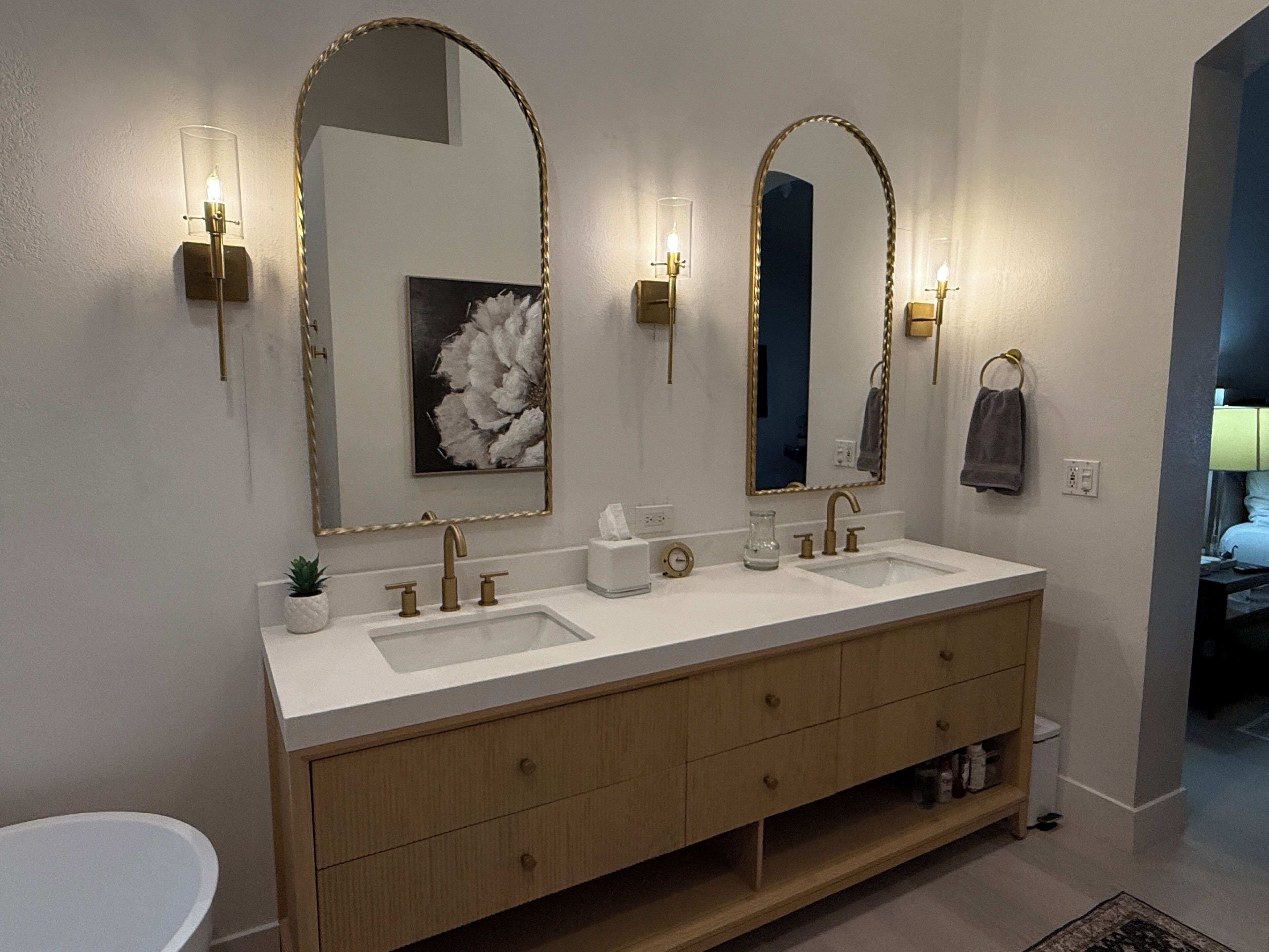Une salle de bain moderne avec un meuble-lavabo à deux vasques, un grand miroir, des appliques murales et une petite plante en pot.