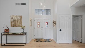 A hallway with a wooden floor, a metal table with a vase, a door with a red and white sign, and a ceiling light fixture. - Prime North Scottsdale location with private pool and hot tub (Scottsdale)