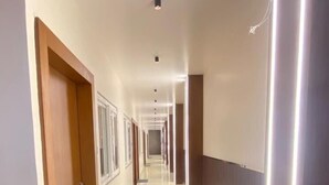 Um corredor comprido e estreito, com uma porta de madeira à esquerda e um candeeiro à direita.