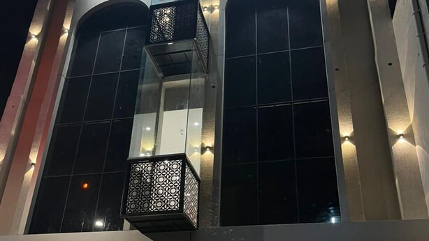 Um edifício moderno com grandes janelas, uma varanda com grades decorativas e um carro estacionado lá dentro.