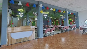 A spacious indoor dining area with multiple tables and chairs, a reception desk, and decorative balloons. - Hotel Om Vilas (Mathura)