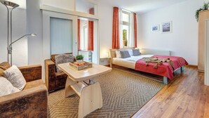 Une pièce confortable avec un lit, un canapé, une petite table agrémentée d’une plante et d’un panier de fruits, ainsi qu’un radiateur.
