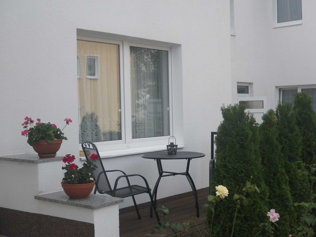 Eine kleine Terrasse mit Tisch und Stühlen, Topfpflanzen und einem Fenster mit Blick zum Himmel.