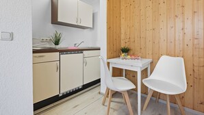 Una cocina compacta con encimera blanca, un lavamanos y una pequeña zona de comedor con dos sillas blancas y una mesa.