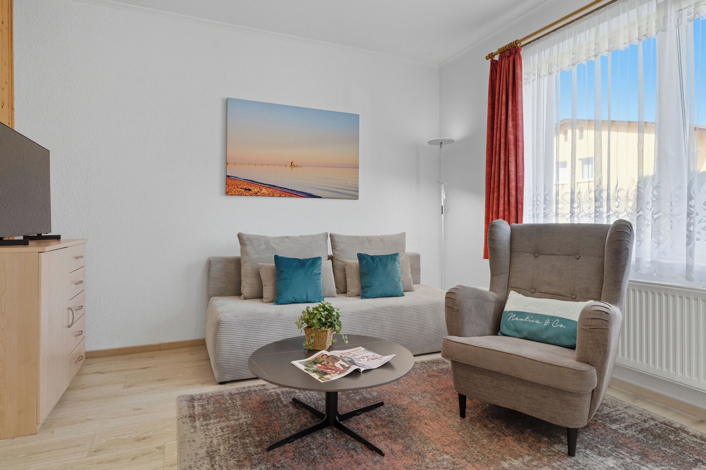 En moderne stue med sofa, lænestol og sofabord, med et maleri, en plante og et magasin.