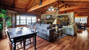A spacious living area with a wooden ceiling, a stone fireplace, and a dining table with chairs. - Canyon Lake Haven Cabin Hot Tub Yard BBQ Fire Pit (Canyon Lake)