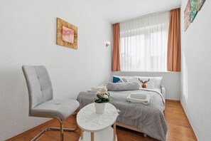 Un dormitorio moderno con cama, una silla, una mesita con una planta y una ventana con cortinas.