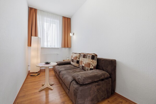 Une petite pièce agréable, avec un canapé marron, une petite table, une lampe et une fenêtre avec des rideaux.