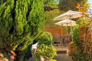 Un espace patio agrémenté d’une pergola en bois, de deux parasols, ainsi que d’une table et de chaises.