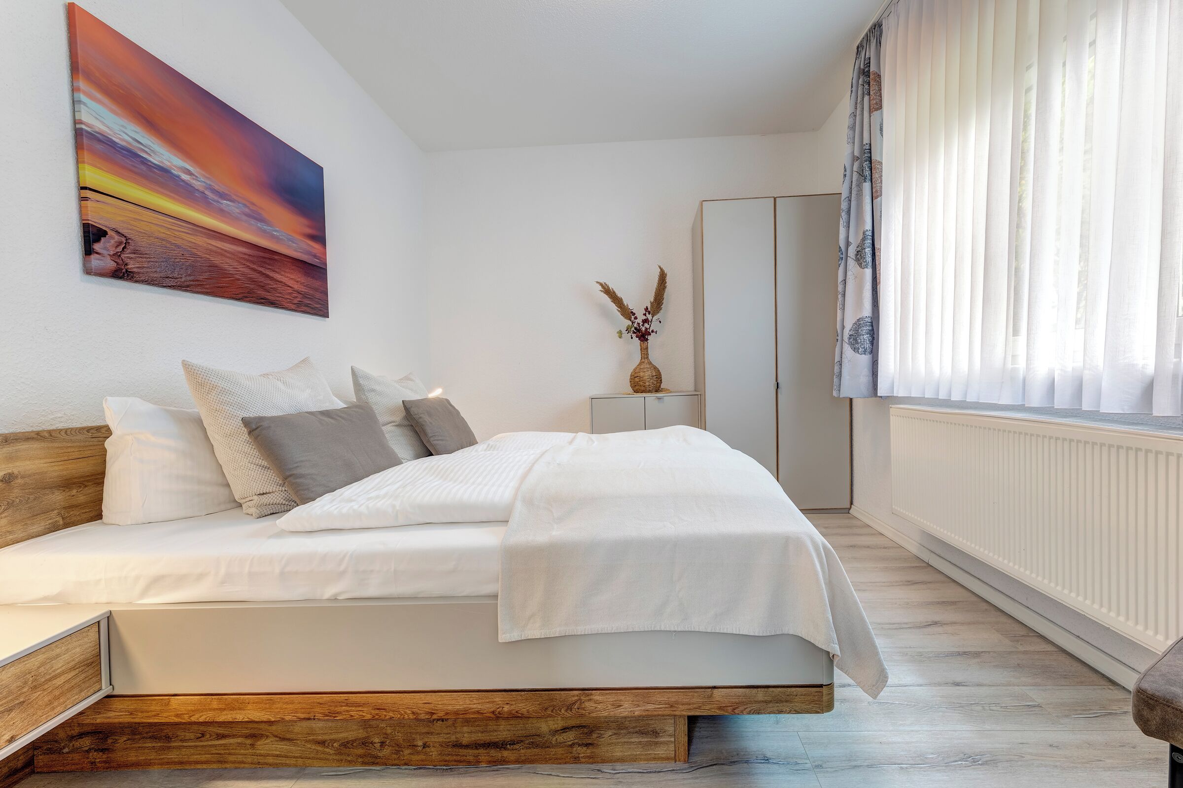 Quarto com cama, mesa de cabeceira, penteadeira e janela com cortinas.