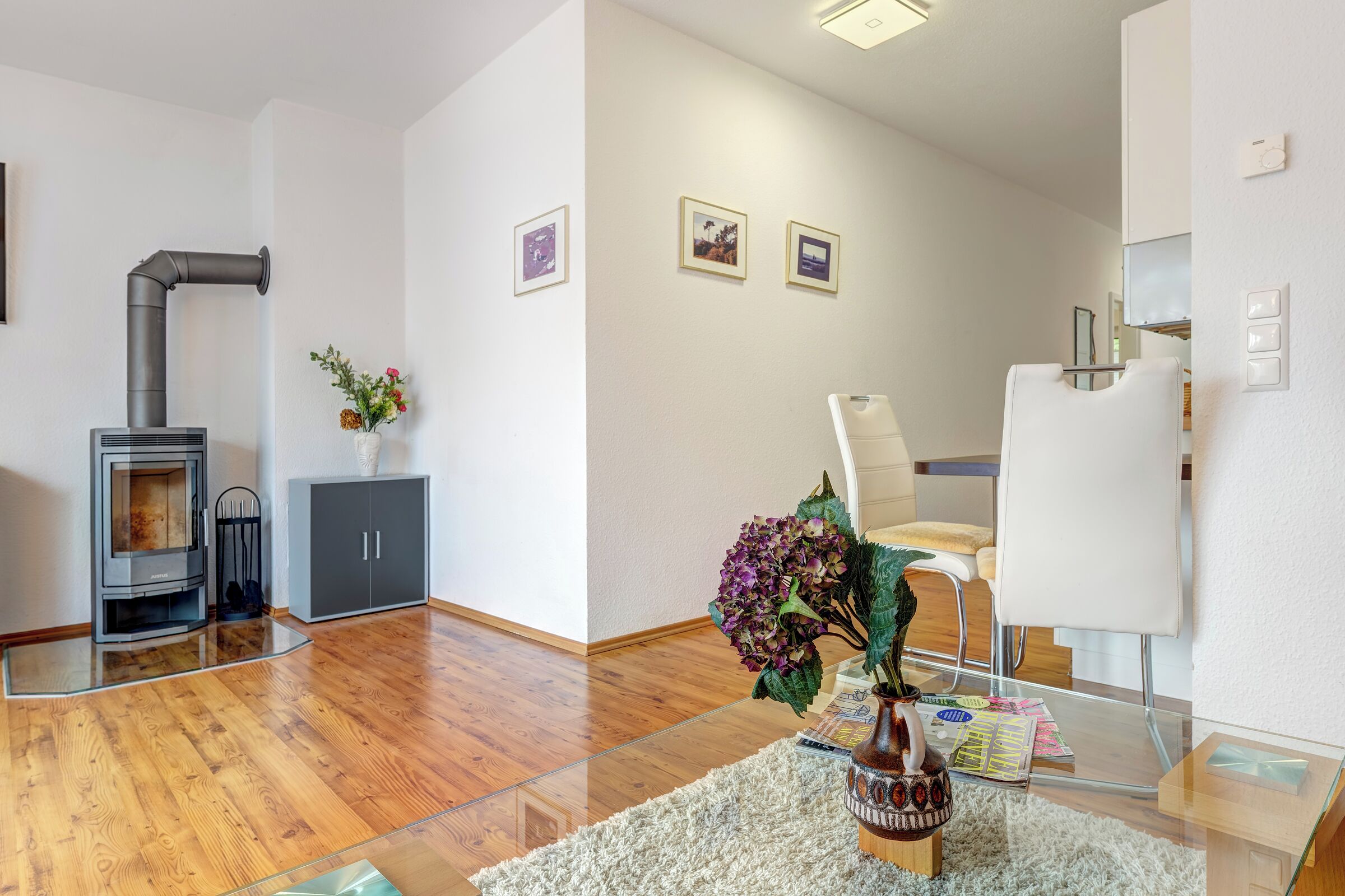 Een moderne woonkamer met een houtkachel, een glazen salontafel en een witte fauteuil.