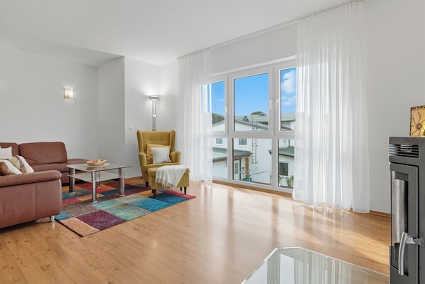 A modern living room with a brown sofa, a yellow armchair, a glass coffee table, and a colorful rug.