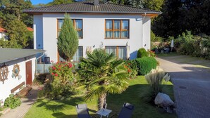 Una casa a due piani con un giardino, una panchina e un tavolino con sedie.