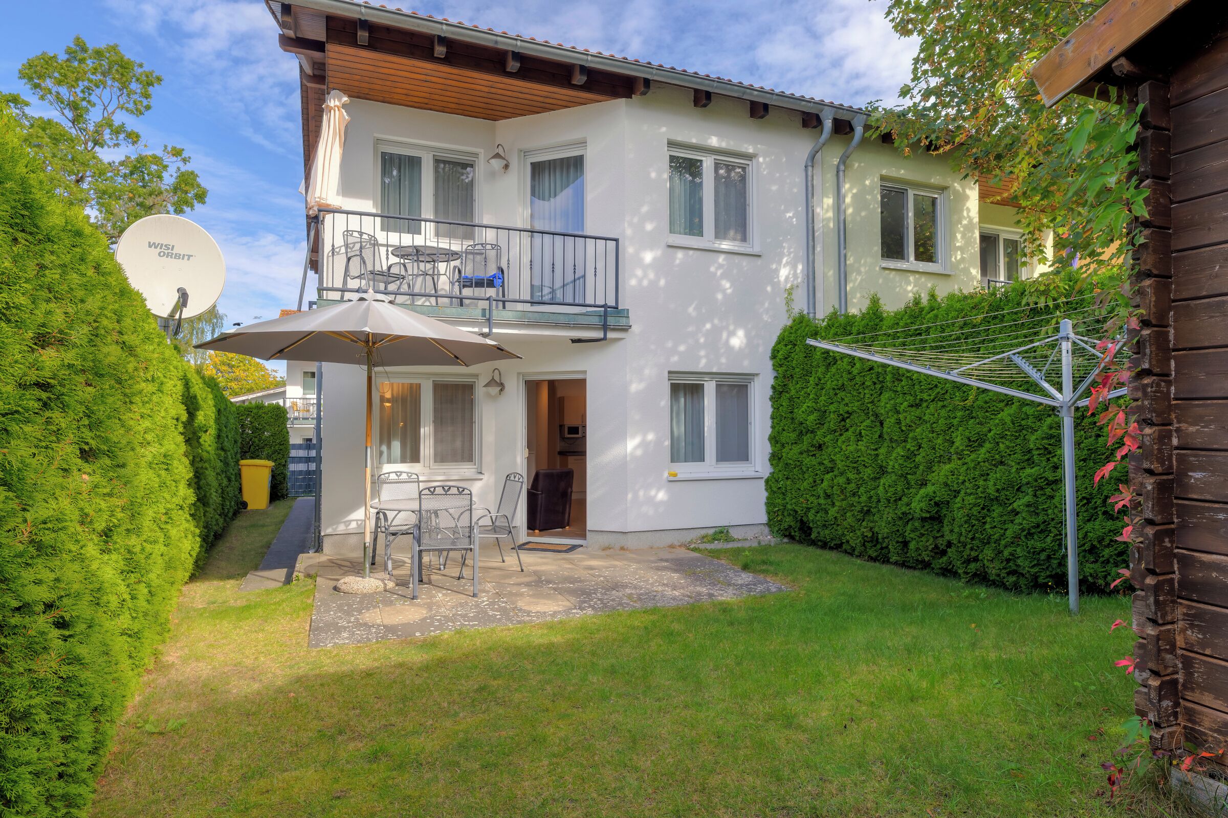 Une maison à deux étages dotée d’un balcon, d’une antenne parabolique et d’une terrasse aménagée avec du mobilier d’extérieur.