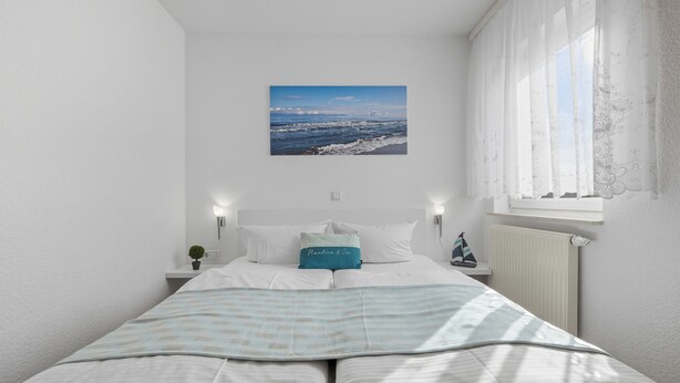 A bedroom with a bed, a window with curtains, a wall-mounted picture, and a bedside table with a plant.