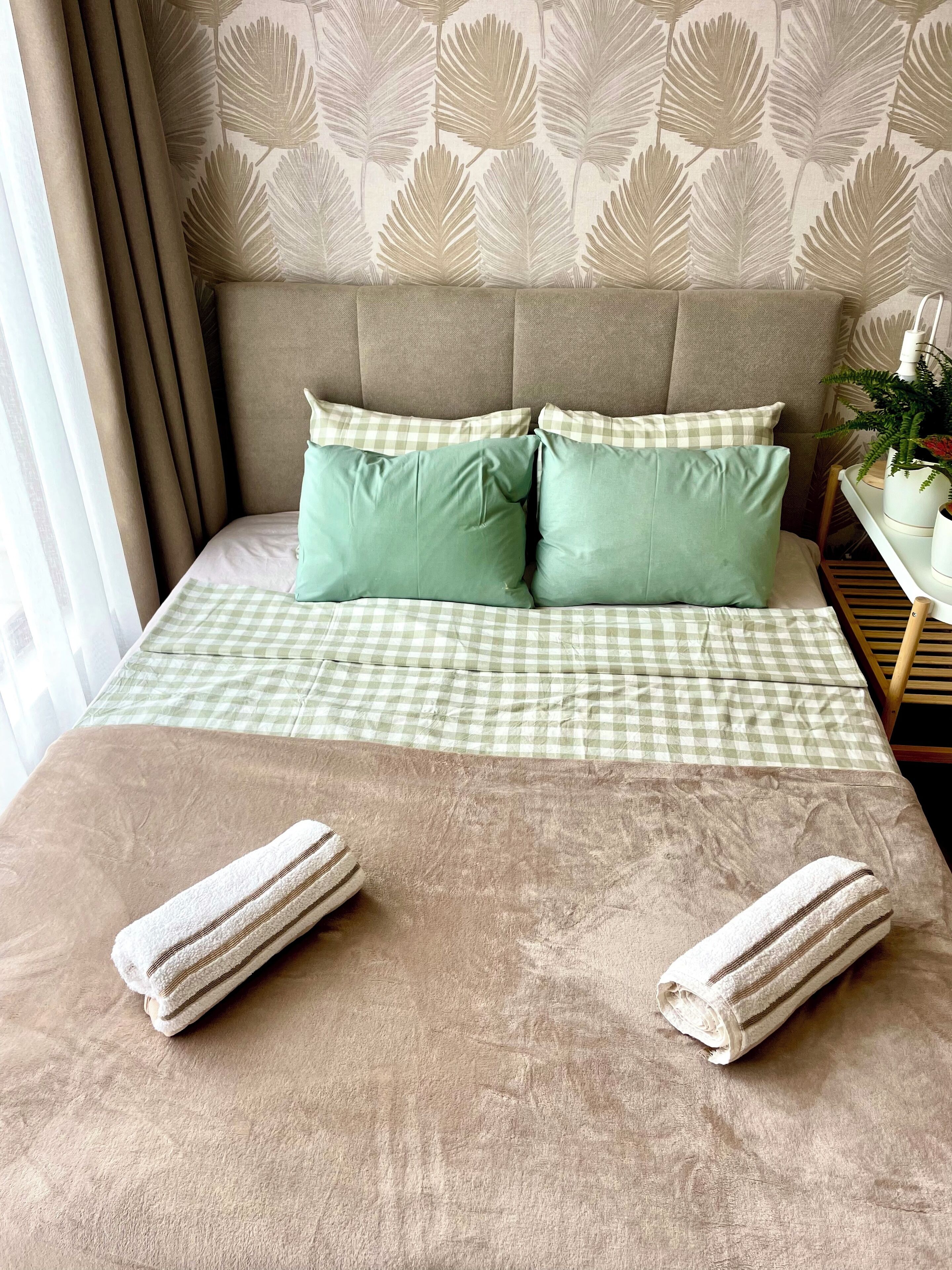 A neatly made bed with a checkered bedspread, two pillows, and two rolled towels.