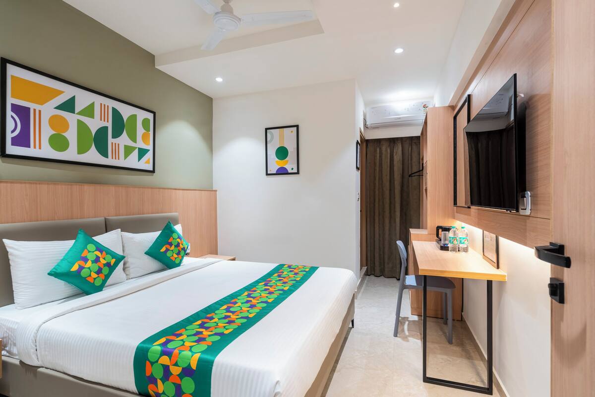 A hotel room with a bed, a desk, a chair, a TV, and artwork on the walls.