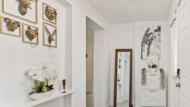 Ein Flur mit weißer Wand, einem Spiegel und einer weißen Konsole mit Pflanzen.