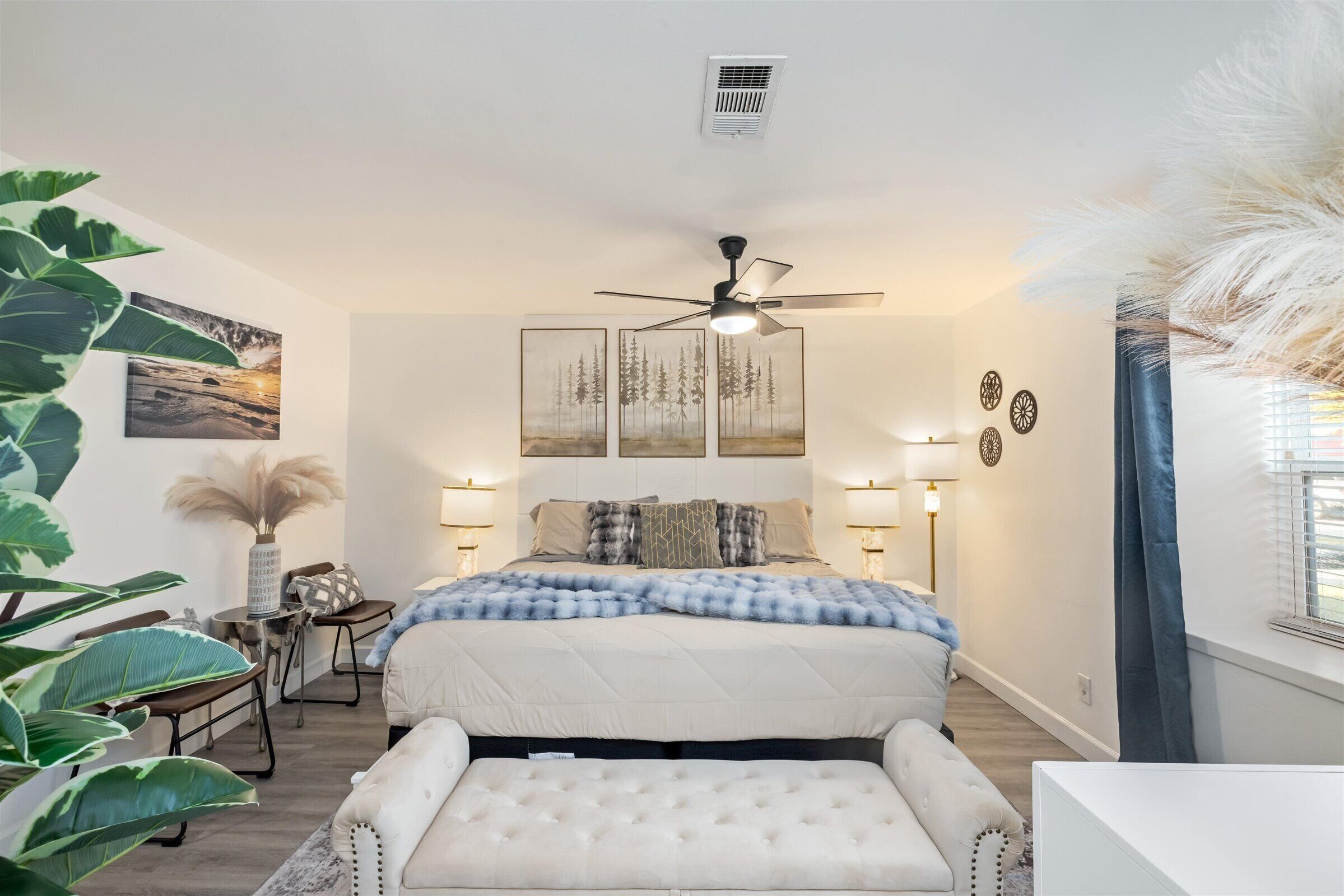 A bedroom with a bed, bedside lamps, a ceiling fan, and a large window with curtains.