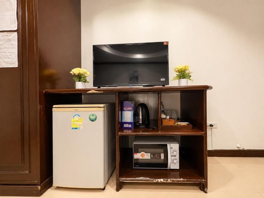 A compact kitchenette with a refrigerator, microwave, and a flat-screen TV on a wooden shelf.