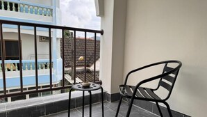 Un balcón con una silla, una mesita pequeña y vistas a un edificio de fachada azul y blanca.