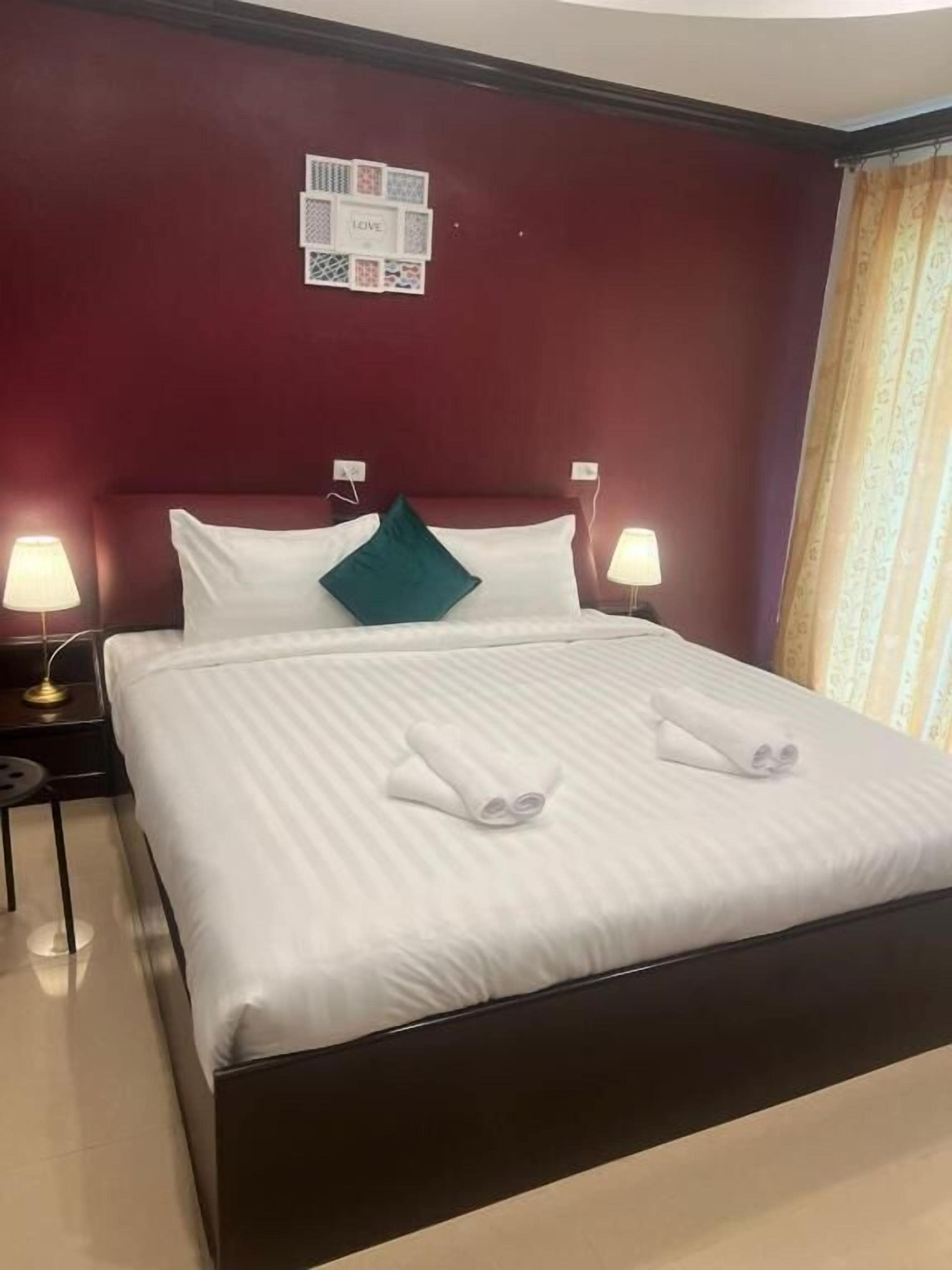 A hotel room with a large bed, two bedside lamps, a red accent wall, and a framed collage above the bed.