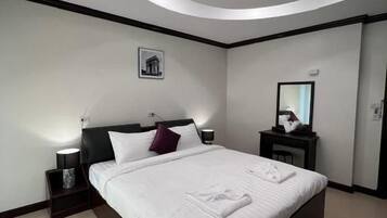 A modern hotel room with a large bed, a nightstand, a bedside table, a wall-mounted mirror, and a ceiling light fixture.