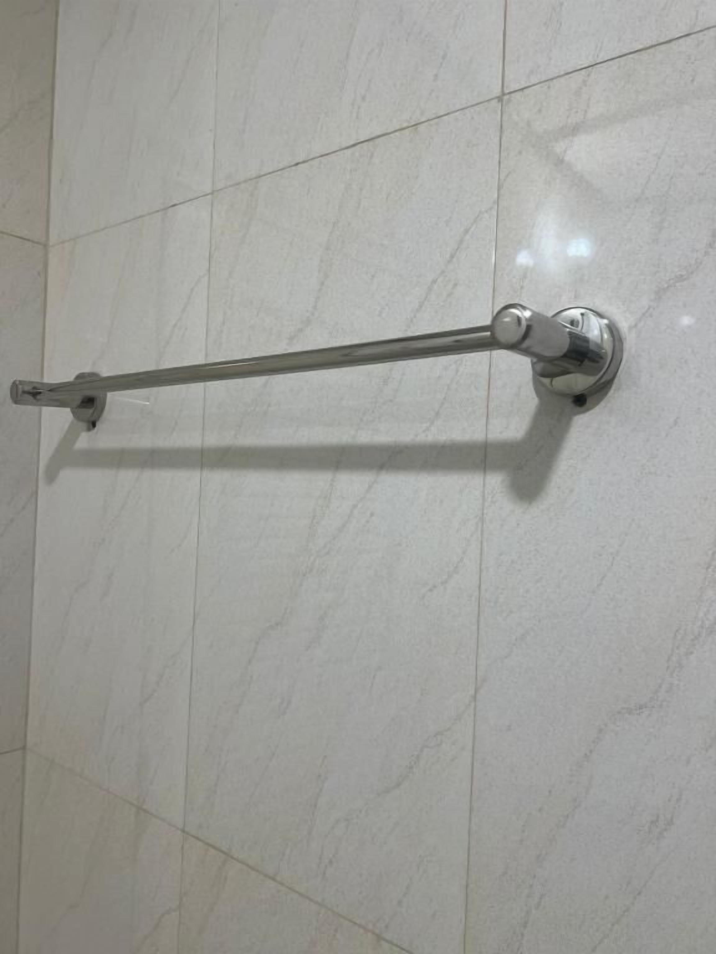 Une salle de bain avec des murs recouverts de carreaux blancs et un porte-serviettes chromé fixé au mur.