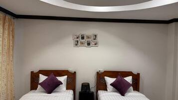 A hotel room with two beds, a ceiling light fixture, and a wall-mounted photo collage.