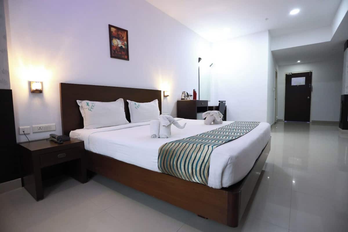 Habitación de hotel con una cama grande, una mesita de noche, un escritorio, una silla, una lámpara, un cuadro en la pared y una puerta al fondo.