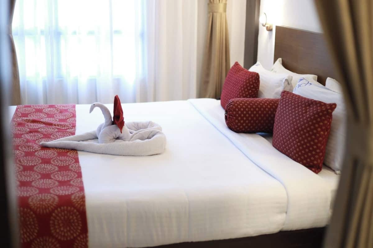 Una cama bien hecha con una toalla con forma de cisne, almohadas rojas y una colcha estampada en rojo.