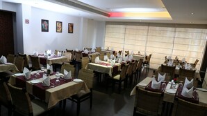 Un restaurant avec de nombreuses tables dressées pour le service, doté de chaises en osier et de nappes blanches.
