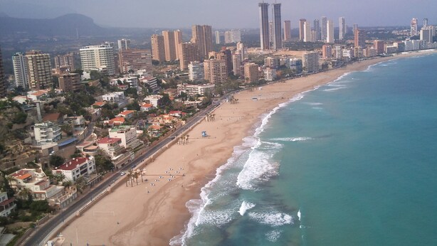 Une vue aérienne d’une ville côtière, avec une vaste plage, de hauts immeubles et une vue dégagée sur l’océan.