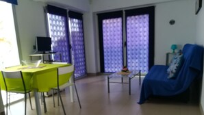 Un salon avec une table verte, un canapé bleu et une petite table sur laquelle est posé un vase de fleurs.