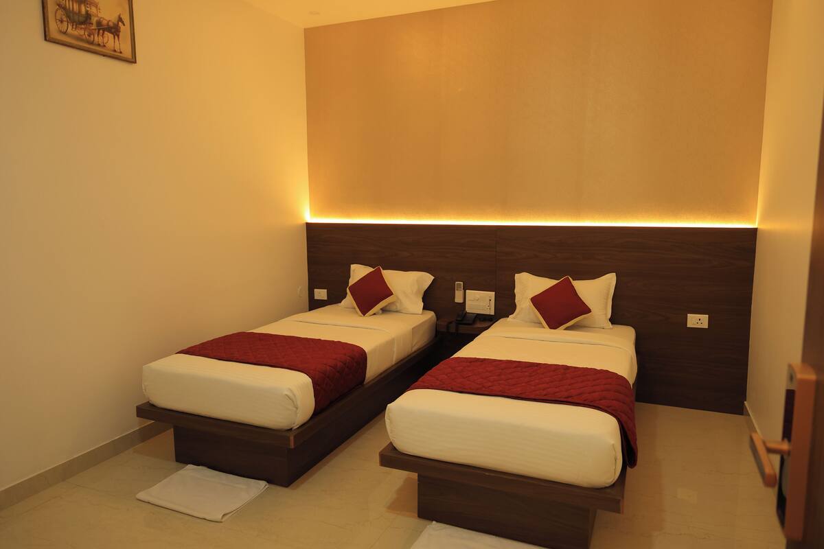 A hotel room with two beds, each with a wooden headboard, white bedding, and red throw pillows.