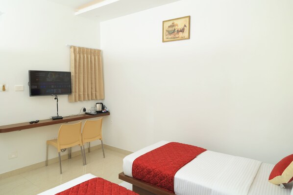 A hotel room with two beds, a desk with a computer, a TV, and two chairs.