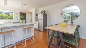 A modern kitchen with a central island, bar stools, a dining table with chairs, a refrigerator, and a round mirror.