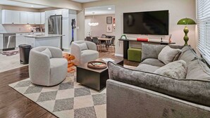 A modern living room with a sofa, a coffee table, and a TV. - Spacious Home In OP|Sleeps 12|5BR|Parking (Overland Park)