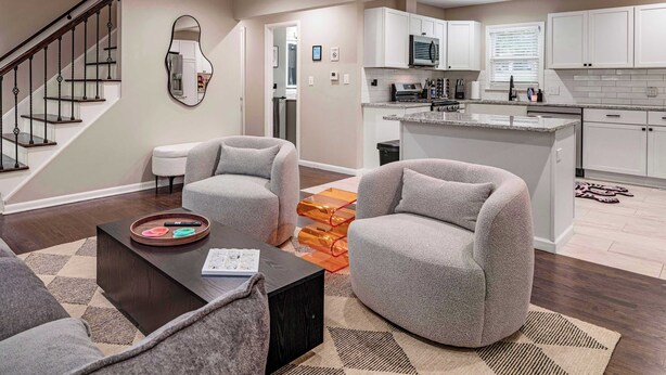 A modern living room with a sofa, coffee table, and a kitchen area with white cabinets and a microwave. - Spacious Home In OP|Sleeps 12|5BR|Parking (Overland Park)
