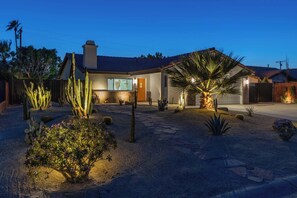 Une maison avec une terrasse en pierre, des cactus et un palmier.
