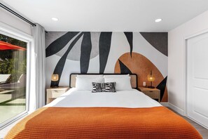 Moderni hotellihuone, jossa on suuri sänky, geometrisesti kuvioitu seinämaalaus ja näkymä ulos.