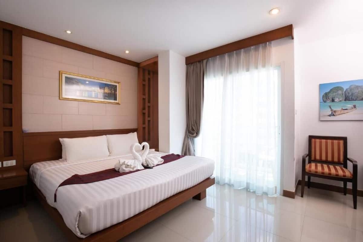 Ein Hotelzimmer mit einem großen Bett, einem Holzkopfende, einem Bild an der Wand, einem Sessel und einem Fenster mit Vorhängen.