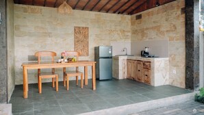 Una cocina con pared de piedra, mesa de madera, sillas, refrigerador y cafetera.