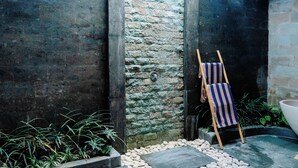 Un muro de piedra con una puerta, un pequeño jardín de guijarros y una toalla a rayas sobre un caballete.