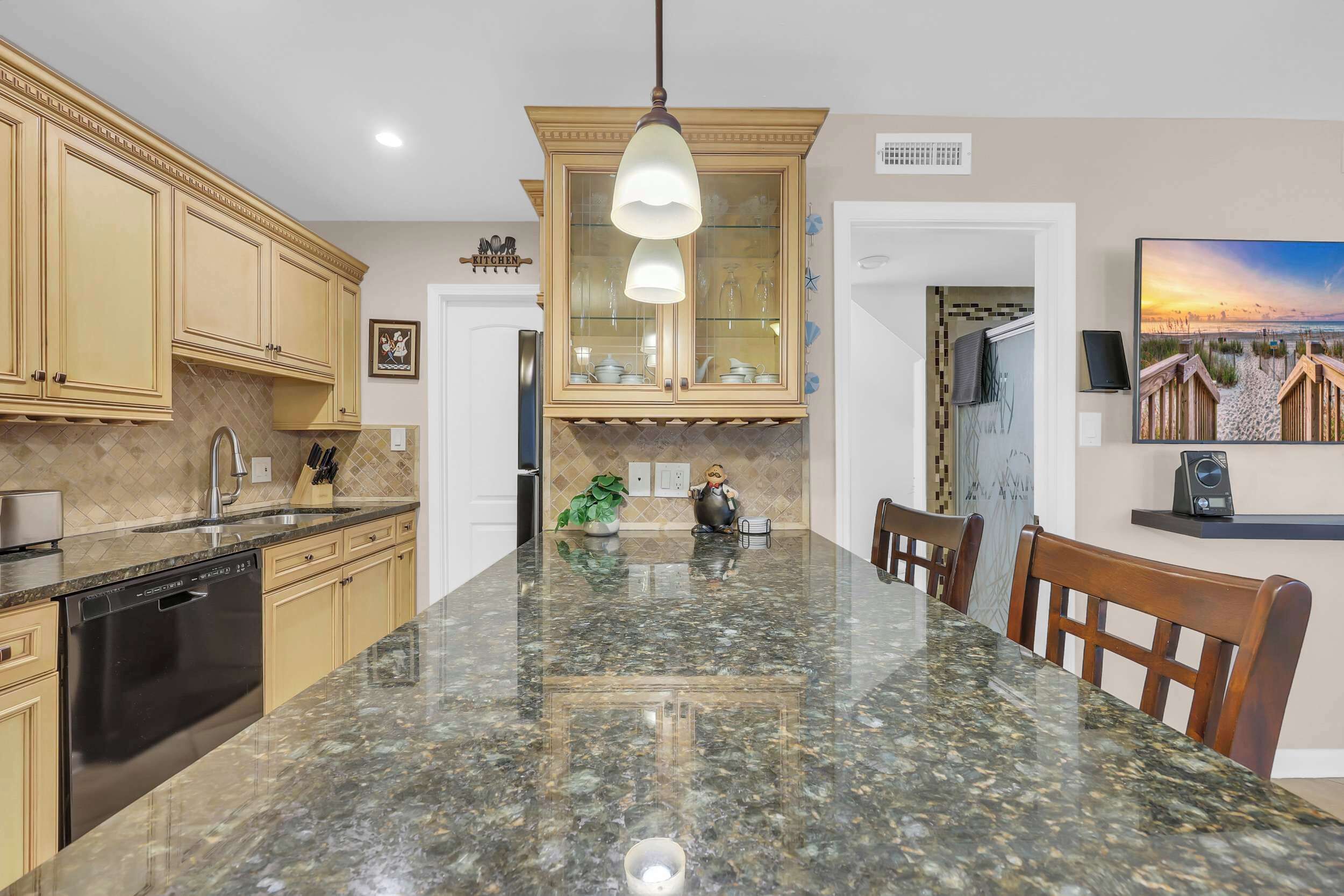 A kitchen with a granite countertop, wooden cabinets, a dishwasher, and a hanging light fixture.