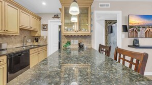 A kitchen with a granite countertop, wooden cabinets, a dishwasher, and a hanging light fixture. - Driftwood Days Pet Friendly Beach Home (Myrtle Beach)
